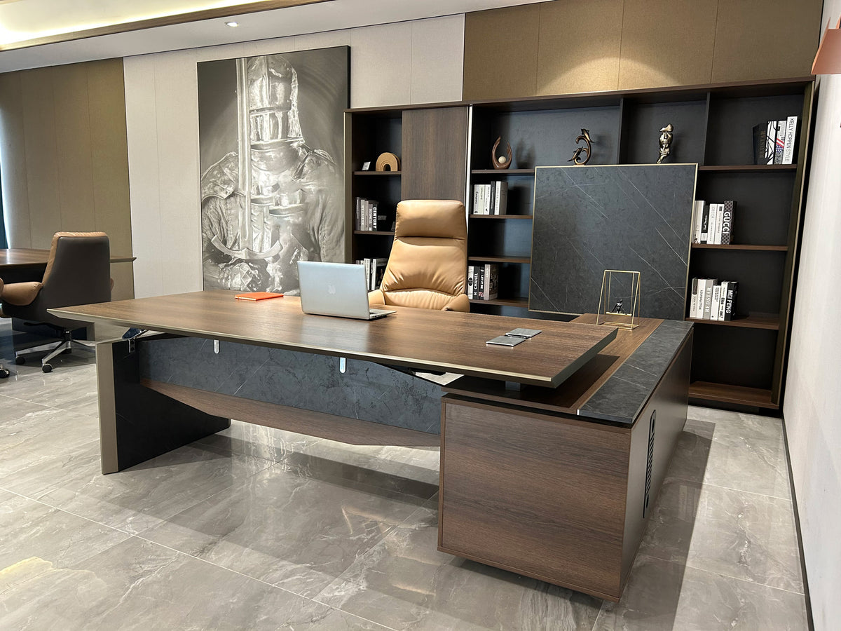 Executive office desk with return in brown oak colour, featuring a desktop thickness of 4cm, metal handles and cable management system, set against a bookcase background.